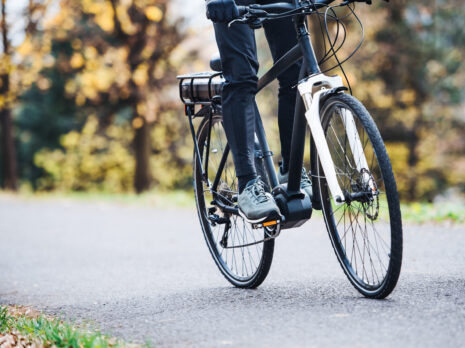 An unrecognizable man on electrobike cycling outdoors on a road in park.
